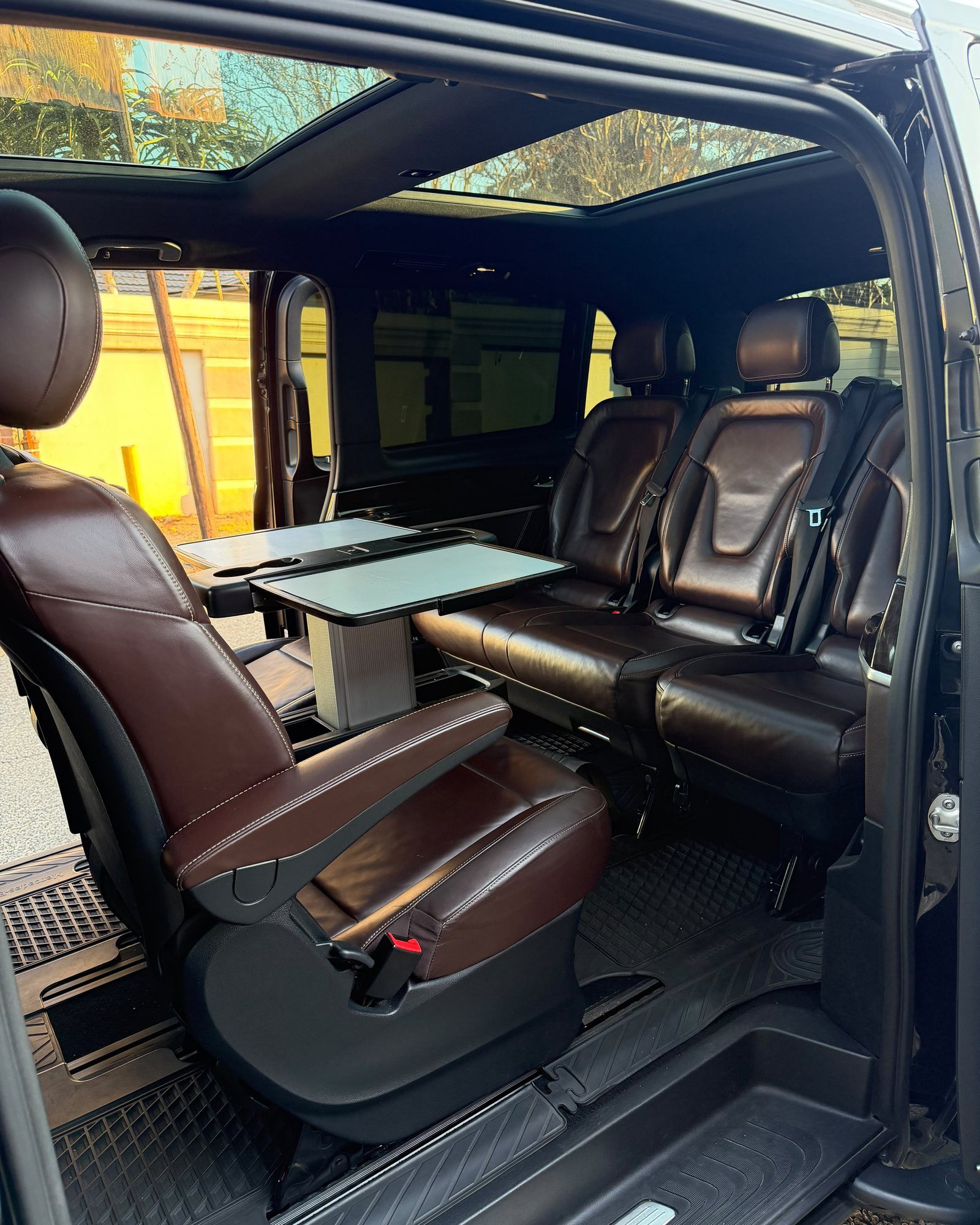The rear cabin of a Foreverlit Mercedes-Benz V-Class — brown leather captain chairs, conference tables and a panoramic roof